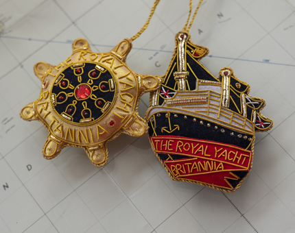 Two embroidered hanging decorations. One is a ships wheel and the other is of Britannia.